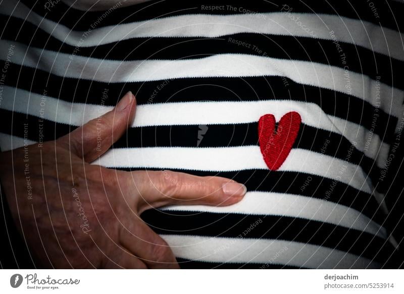 An embroidered red heart on a thirt , with black and white stripes and two fingers pointing to it. heart-shaped Heart Emotions Romance Red Deserted Colour photo