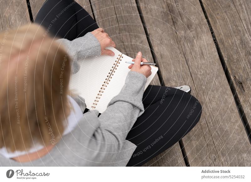 Crop woman writing notes in notebook on wooden pier take note write information copybook planner pastime female casual sit notepad study lifestyle diary