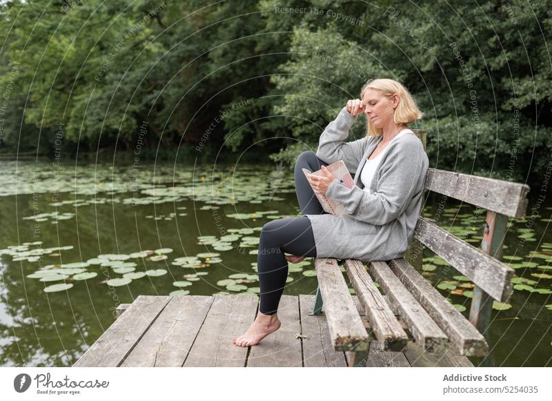 Thoughtful woman with notebook sitting on bench near lake read information copybook park nature tree thoughtful think concentrate female rest planner relax