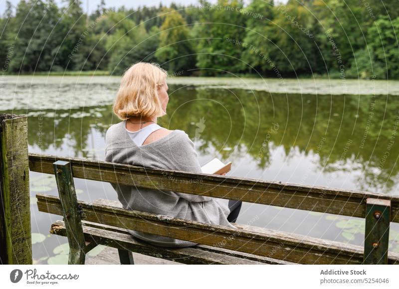Thoughtful woman with notebook sitting on bench near lake read information copybook park nature tree thoughtful think concentrate female rest planner relax