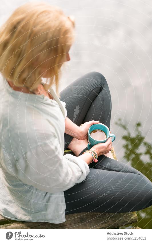 Woman with cup of hot tea sitting near lake woman hot drink recreation pier legs crossed nature aromatic harmony female rest countryside relax beverage coffee