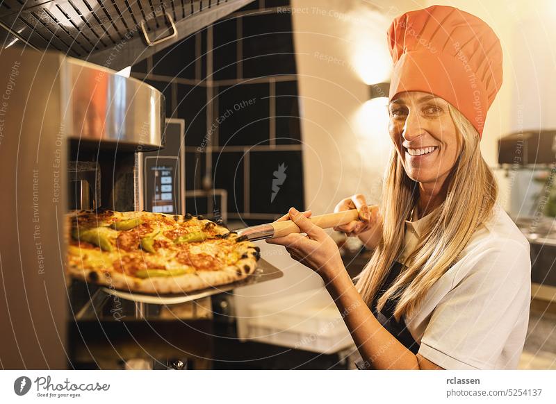 traditional female pizza baker holding a fresh pizza from the stone oven on peel at italian pizzeria woman hat wood fire brick oven chef cook gourmet