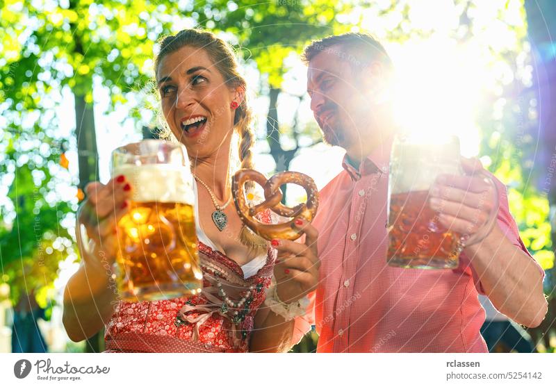 Happy Couple in Beer garden or oktoberfest making party and enjoying a glass of beer and the sun man woman love couple pretzels flirt cutlery bavarian festival