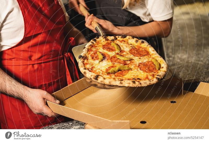 pizza bakers pulling a fresh salami pepperoni pizza from the stone oven in a box for delivery at italian pizzeria hovel tasty cheesy man delivery service smile