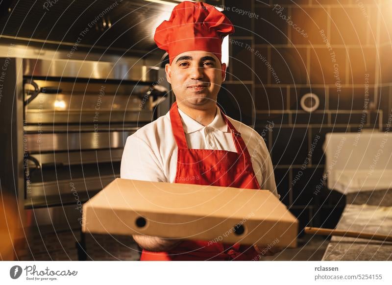 italian pizza baker holding packet pizza in a box for delivery at italian pizzeria apron tasty cheesy man salami delivery service smile happy hat wood fire
