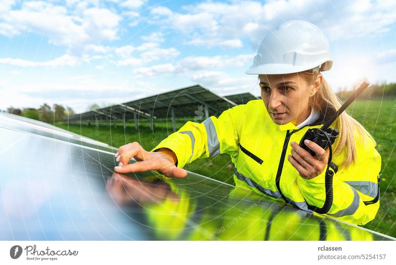 Female engineer looks skeptical to a solar panel and holding a walkie talkie to communicate. Sustainable energy and solar power field concept image speak