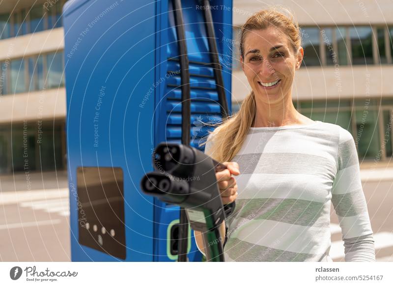 Beautiful woman holding a DC CCS2 EV charging connector on a Hypercharger or Supercharger for recharge her car. happy female nfc debit card payment paying rfid