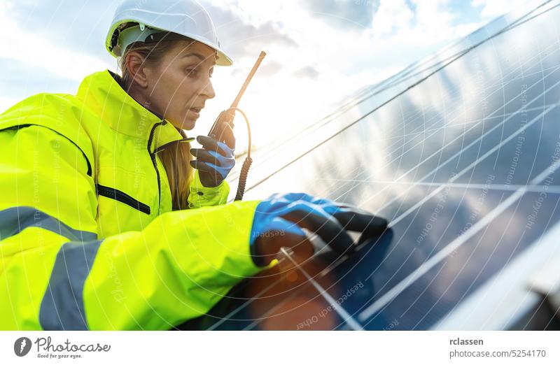 Female engineer talking in a walkie talkie to control a solar panel field and looks happy. Sustainable energy and solar power field concept image speak