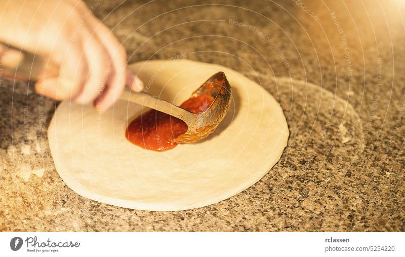 Pizza maker preparing raw pizza with tomato sauce and spoon in the italian pizzeria prepare ketchup tomatoes hand dough wood fire brick oven chef cook gourmet