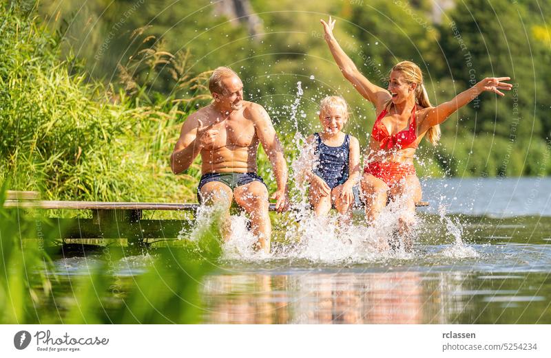 Happy family bathing and splashing water with their foot at jetty on a river in summer reed vacation swimwear bikini bavaria germany landing stage lake happy