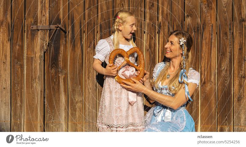 Mother and daughter holding milk cans in traditional Bavarian Tracht at a farm in Bavaria on a wood background. Oktoberfest concept image braid girl child