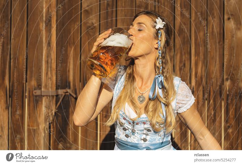 Girl in traditional Bavarian Tracht drinking beer out of a huge mug in Bavarian beer garden or oktoberfest woman gold party restaurant alcohol beverage toast
