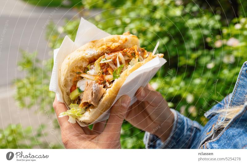 Woman holding a Doner Kebab (sandwich) in Germany famous kebab fast food snack in flatbread. hand restaurant eat fresh woman chicken meat salad tomato healthy