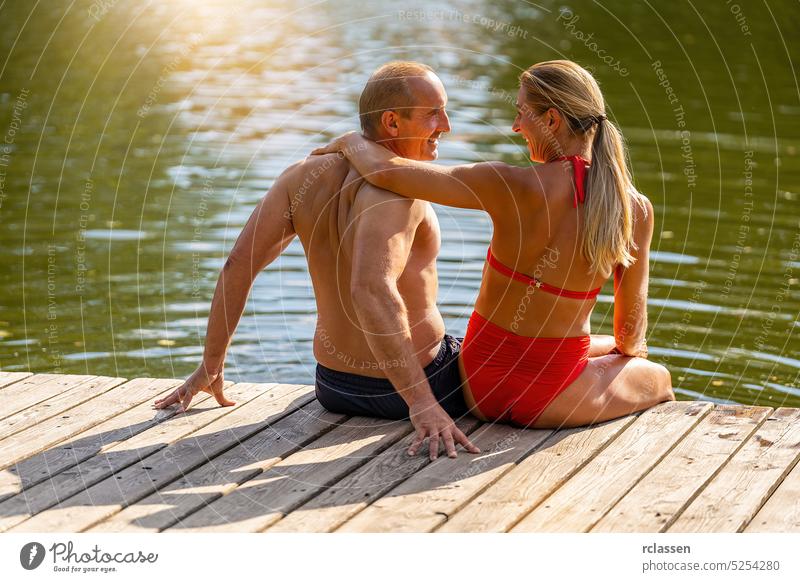 Mother and father enjoy the summer at jetty on a lake in summer love hug man male reed vacation swimwear bikini bavaria germany landing stage river happy fun