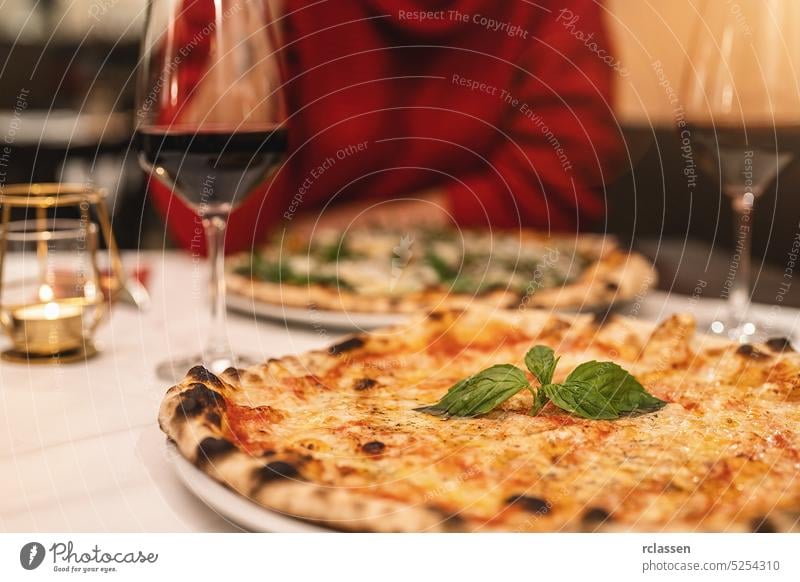 people drinking red wine and eating margherita pizza with basil in a italian restaurant couple rendezvous slice cheese london new york taste friends winery