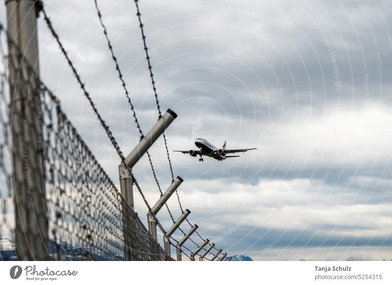 Airplane approaching over the barbed wire landing approach Fence Barbed wire cloudy Passenger plane Airport Border Boundary Aviation Flying Exterior shot Sky