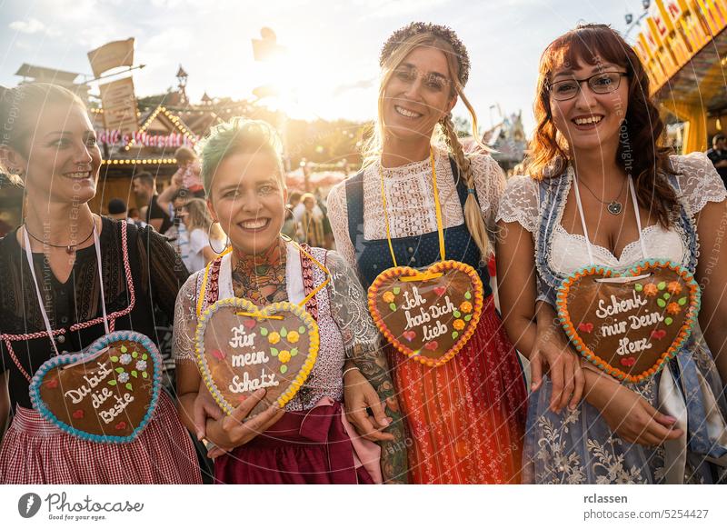 Friends visiting together Bavarian oktoberfest in Dirndl with Schenk mir dein Herz, Für mein Schatz, Ich hab dich lieb (German: Give me your heart, For my sweetheart) written on gingerbreads heart