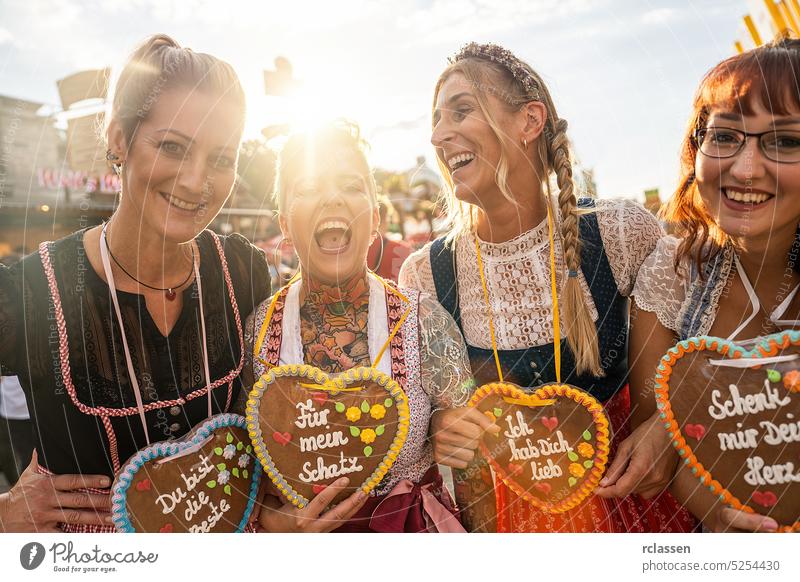 women in traditional Bavarian clothes dirndl with a Schenk mir dein Herz, Für mein Schatz, Ich hab dich lieb (German: Give me your heart, For my sweetheart) written on gingerbreads heart, Oktoberfest