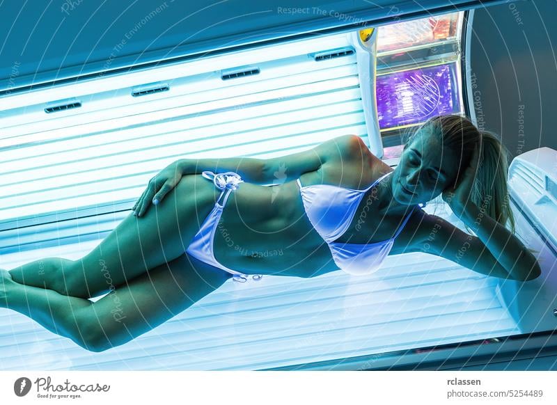 sexy woman in a bathing suit sunbathing in a solarium under the ultraviolet rays tan bed salon skin girl women vertical relax people summer spring light spa