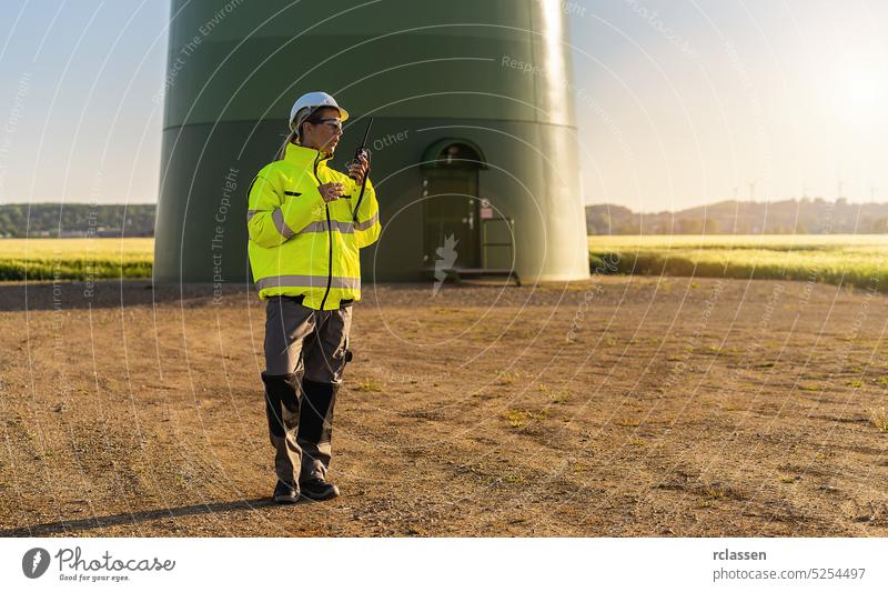 female engineer with safety jacket standing in front of a wind turbine using walkie talkie to checking wind turbine system at a new energy farm engineering