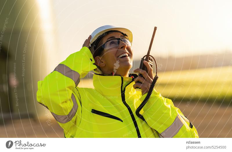 female engineer with safety jacket standing in front of a wind turbine talking in a walkie talkie to checking wind turbine system engineering field electricity