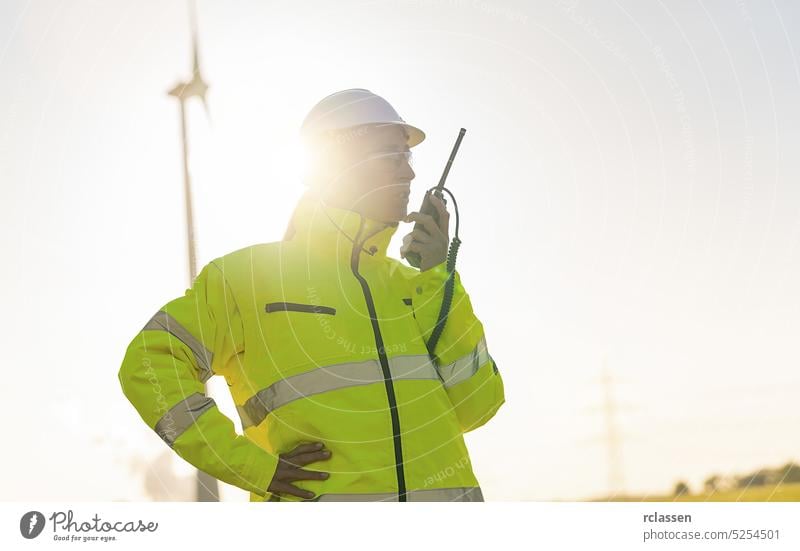 female engineer with safety jacket using walkie talkie to checking wind turbine system at new enegry farm engineering field electricity worker radio talking