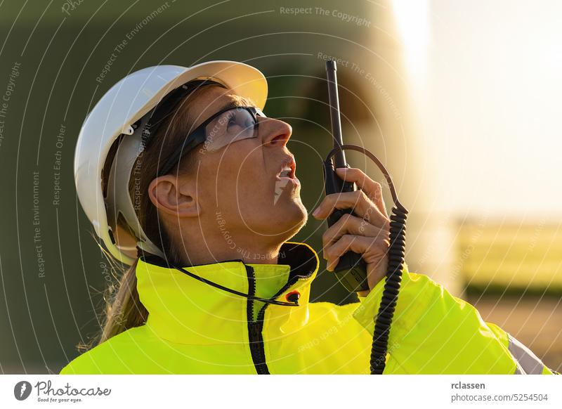 female engineer talking skeptical in a walkie talkie to checking wind turbine system at windfarm safety jacket engineering field electricity worker radio