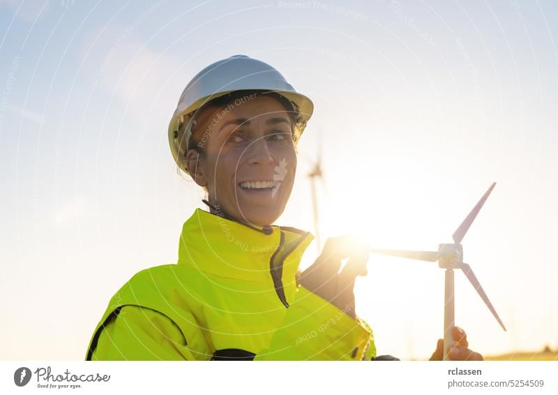 happy female engineer holding wind turbine model looking and checking wind turbines. New Energy concept image sunset safety jacket helmet woman farm hardhat