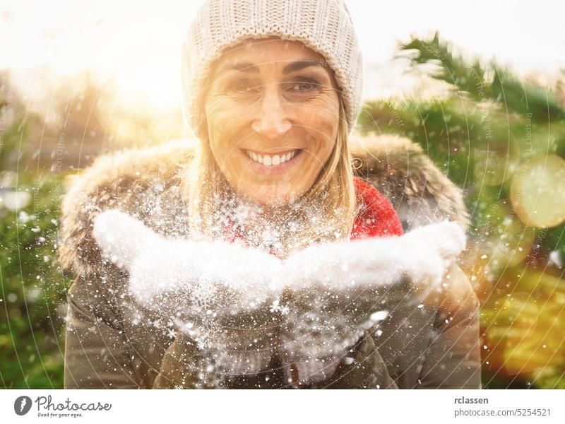 Winter Girl Blowing Snow in frosty winter Park and smilling.  woman Having Fun in Winter time at christmas gloves fir tree christmas tree snow happy people