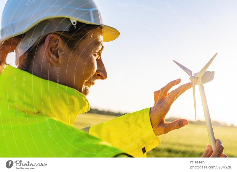 female engineer holding wind turbine model and play with propellers at sunset safety jacket helmet woman farm hardhat technician people business sky technology