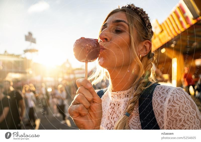 Woman eating candy apple at Oktoberfest wearing Dirndl in germany sweet sugar red woman party oktoberfest beergarden dirndl girlfriends decoration laughing