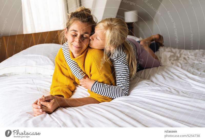 Little girl kissing her mother lying on bed and enjoy the time at home. Mother's Day or mother's love concept image mom family daughter happy mother kid