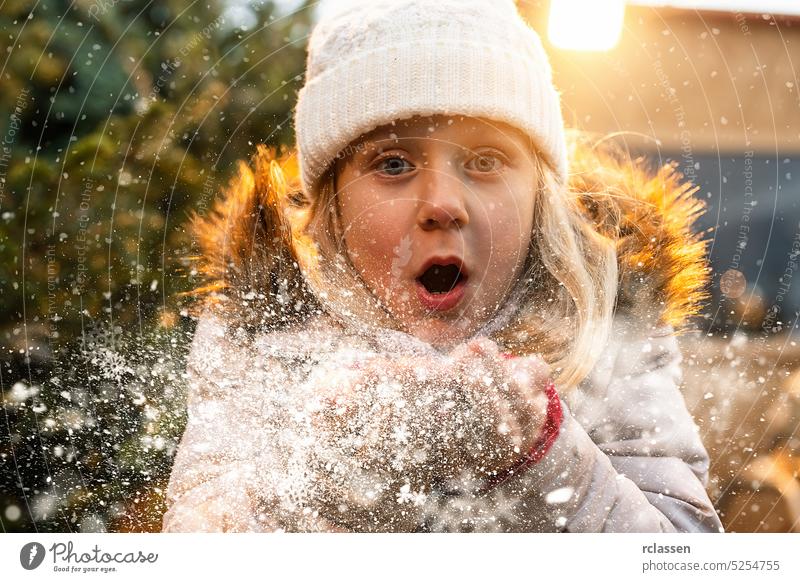 Little girl Blowing Snow in frosty winter Park and smilling. child Having Fun in Winter time at christmas young teenager kid gloves fir tree christmas tree snow