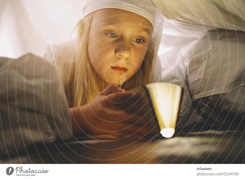Cute girl reading book under blanket at night. Magic light coming out of book. child flashlight kids family home education happy cute bedroom fun learning