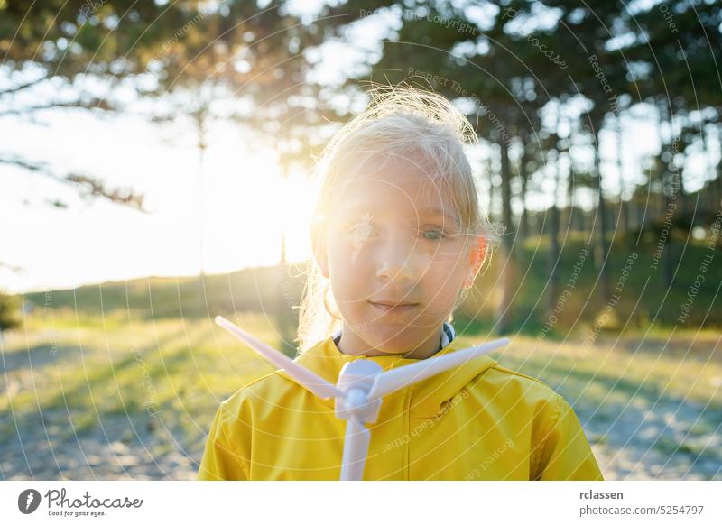 Blonde child holding wind turbine model at sunset at the forest looking at camera. New Energy Production concept image alternative energy innovation childhood