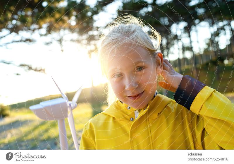 Smiling child holding wind turbine model at sunset at the forest smiling at camera. Energy Production with clean and Renewable Energy concept image