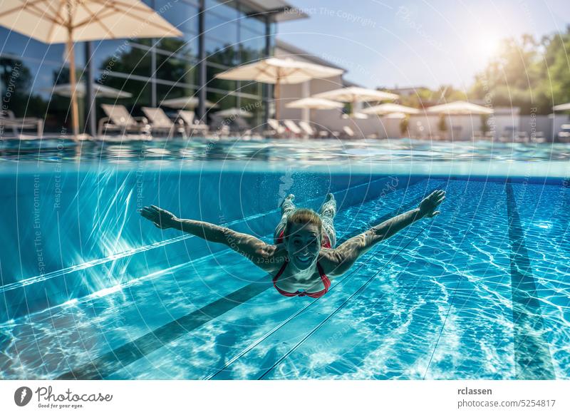 Above and underwater photo of a woman swimming in swimming pool at a hotel or spa resort parasol lounger above half split thermal splash smiling fashion