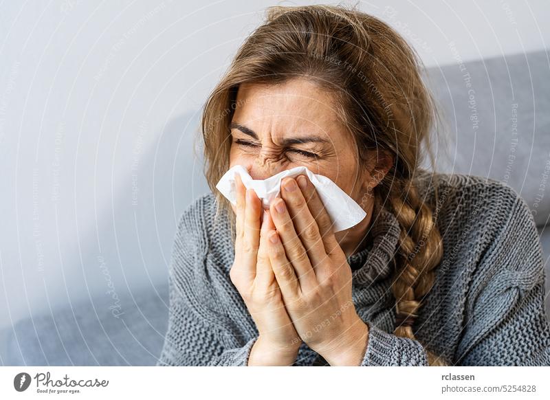 Woman sneezing in a tissue in the living room. Flu, Medicine and healthcare concept image flu allergy woman influenza cold vaccine nose sinus season fever sick