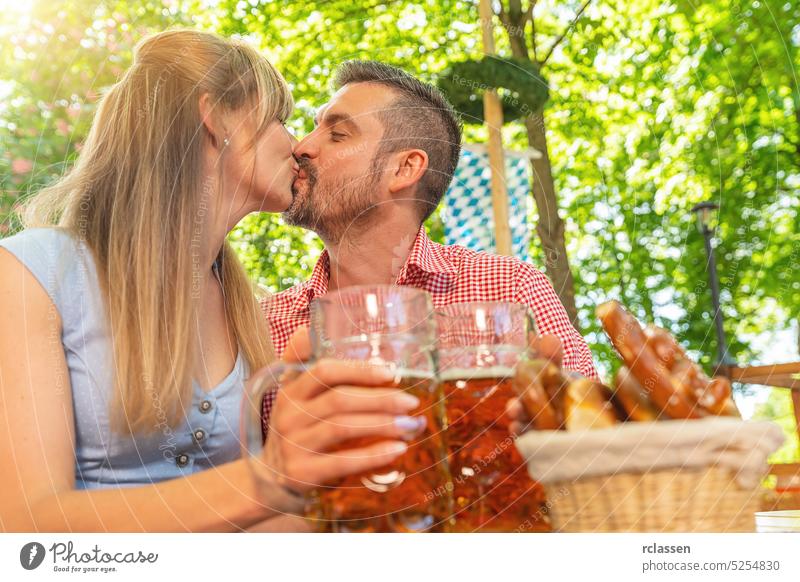Couple kissing and clinking glasses with mug of beer in Bavarian beer garden or oktoberfest couple romantic love friends brezen bavarian festival lederhosen