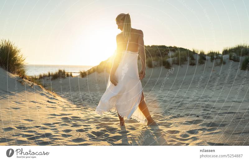 woman stands barefoot through sand dunes towards to sea at summer sunset energetic hippie boho sundown adventure alone beautiful beauty desert dress fashion