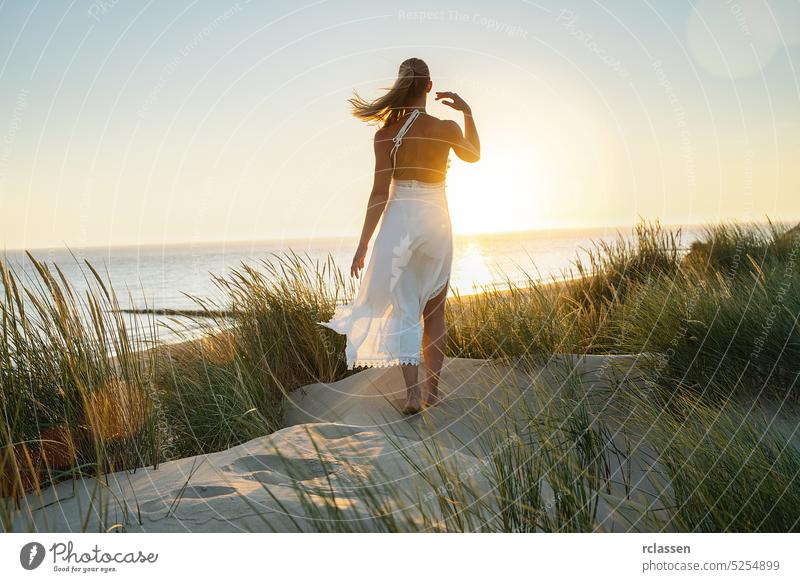 beautiful woman walks barefoot through sand dunes towards to sea at sunset energetic hippie boho sundown adventure alone beauty desert dress fashion free