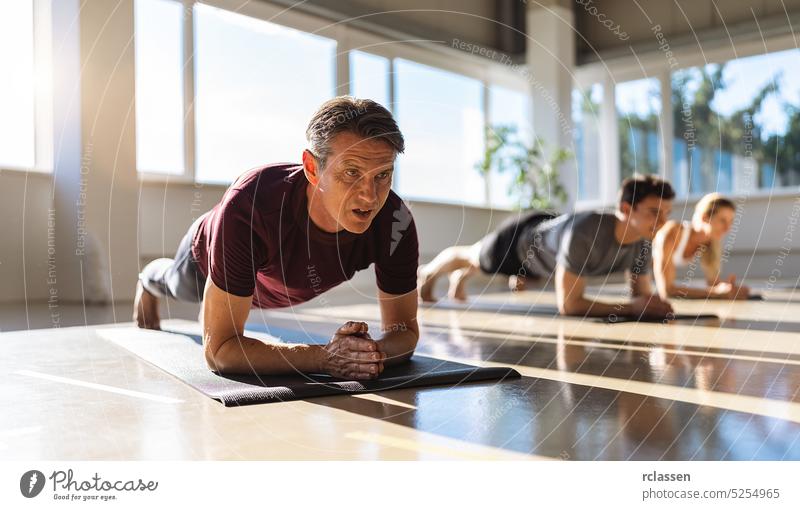 muscular man and woman doing planking exercises in gym on a yoga mat position on elbows while training in studio group workout core fit muscle body male athlete