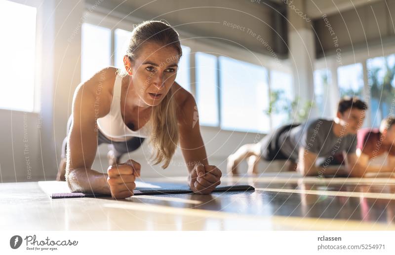 Fitness woman doing plank exercise workout in a group of people in gym. Sport girl and men in sportswear doing exercising on yoga mat, planking indoors core fit