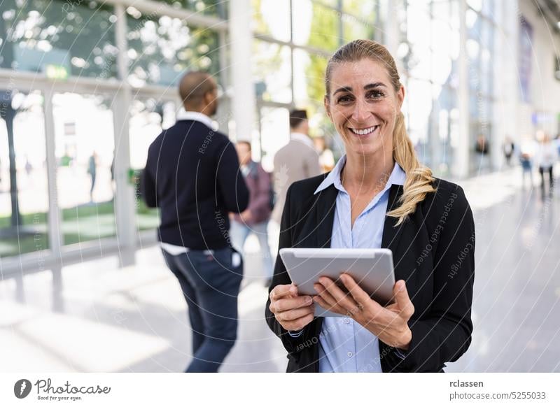 beautiful businesswoman at a trade show trade fair booth visitor communication application job tablet smartphone business woman airport exhibition crowd blurred