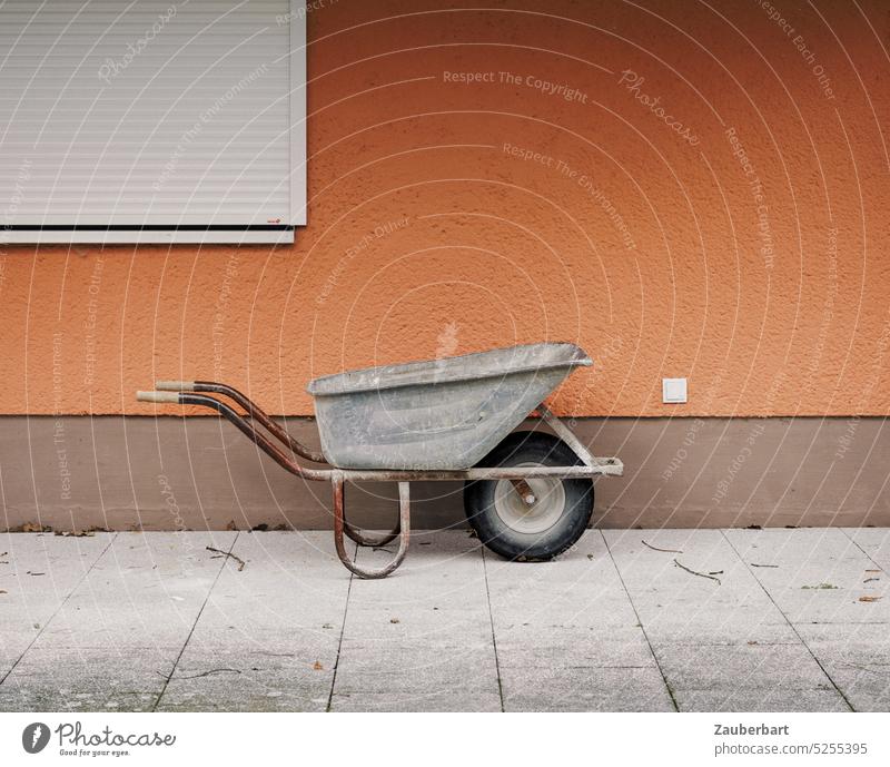 Wheelbarrow in front of orange wall with closed blind as minimaoist symbol of hand and garden work pushcart Cart Orange Terrace Wall (building) minimal