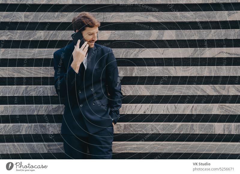 Businessman in elegant black clothes phones to partner focused down keeps smartphone business internet technology businessman mobile formal connection