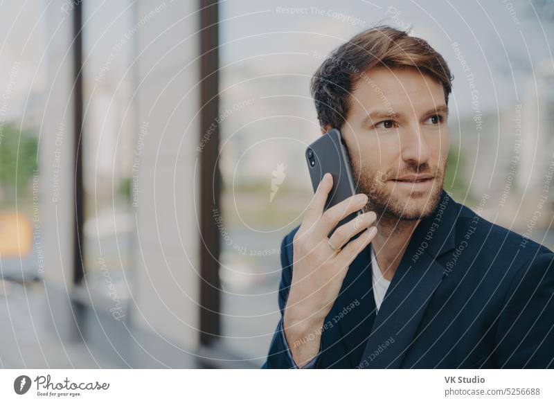 Pensive male entrepreneur focused into distance makes answering call uses mobile phone business man technology businessman formal connection communication