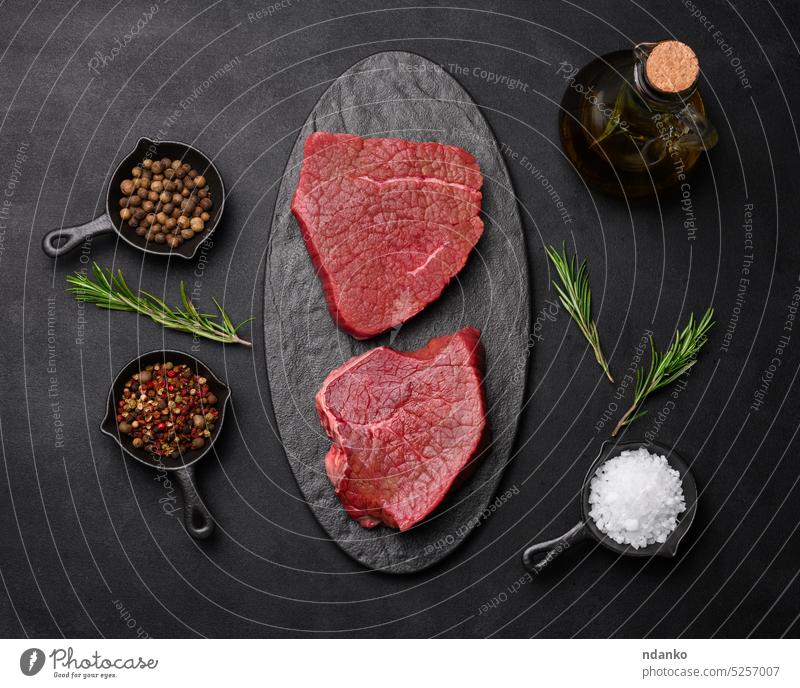 Raw piece of beef with spices pepper, rosemary sprig, salt and olive oil on a wooden board, black background. meat nobody preparation protein raw red seasoning