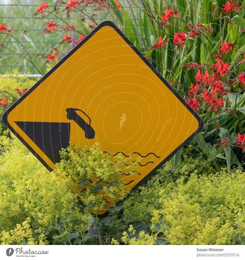 Yellow traffic sign warning about car falling into water in yellow and red flowers Road sign Exterior shot Warning sign Risk of collapse