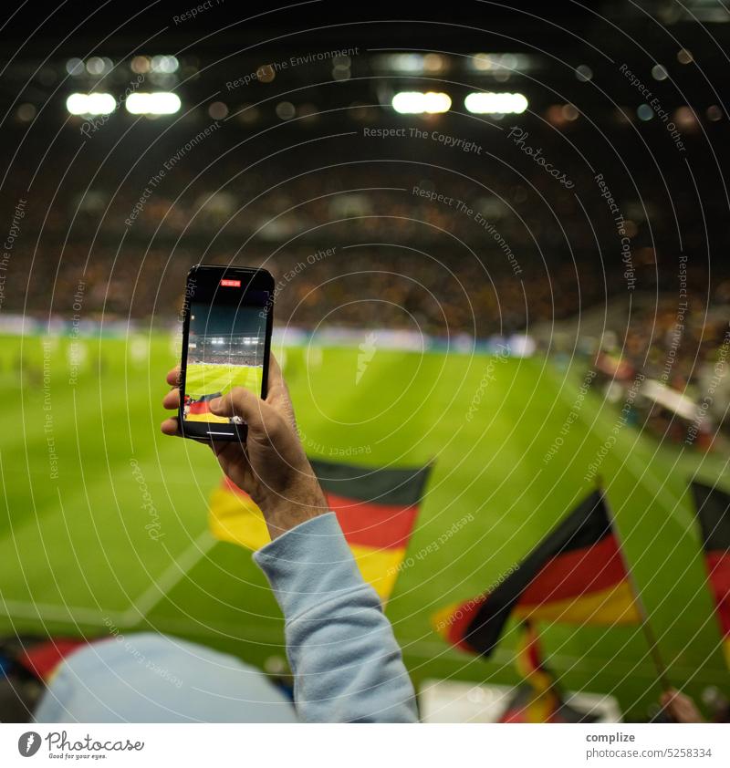 A football fan films with his smartphone a football match in the stadium with waving German flags for the European Championship or World Cup Fans Filming